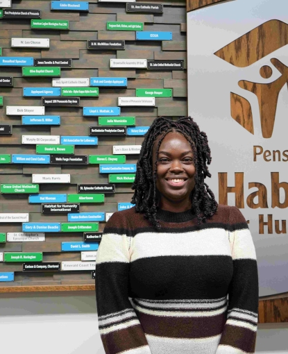 A girl standing in front of a sign for Habitat For Humanity.