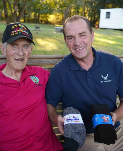 two men sitting together outside on a swing. One man is holding two pairs of socks.