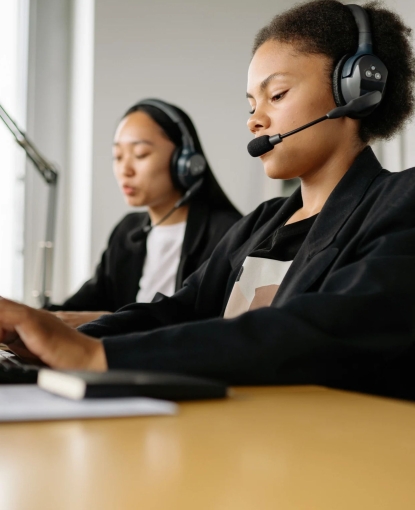 Two women typing on keyboards with a headset on.