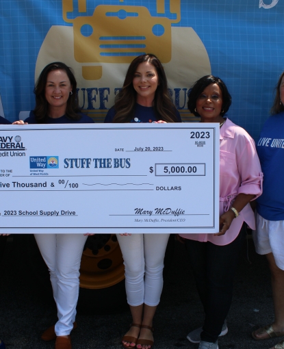 Navy Federal Employees holding $5,000 check in front of Stuff the Bus Bus